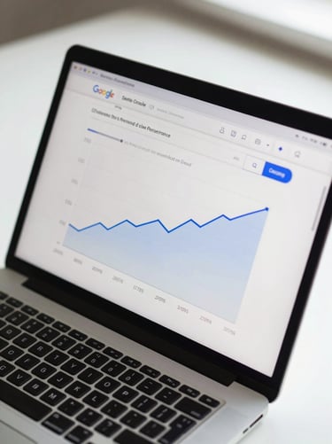 Overhead view of a laptop screen showing a Google Search Console performance graph with organic clicks trending upward over twelve months, soft diffused daylight, clean desk surface visible