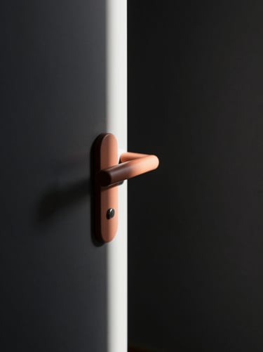 An abstract architectural study focusing on the play of light. A thin strip of light cutting through a dark charcoal (#333333) hallway, illuminating a terracotta (#BC6C47) door handle.