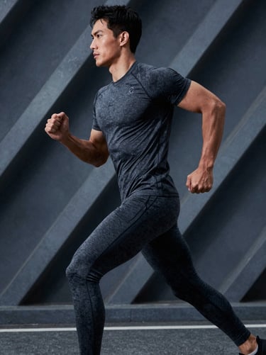 A dynamic shot of a male model in motion, wearing dark graphite activewear, set against an industrial AI-generated background of geometric metal structures and cool blueish-grey shadows.