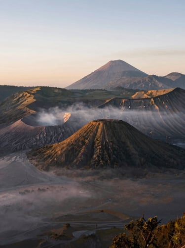 The majestic Mount Bromo caldera at sunrise, soft morning mist blanketing the volcanic sand sea, quiet and vast landscape.