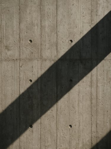 Close-up of a raw concrete wall showing formwork texture and sharp shadows from natural sunlight.