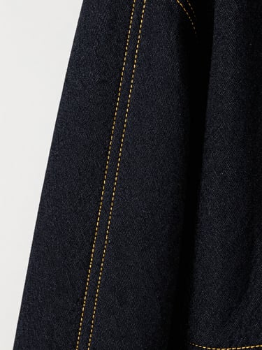 Macro shot of high-contrast gold stitching on dark denim fabric, showing millimeter tolerances and technical precision, 85mm