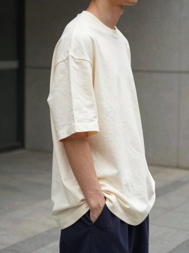 Model in a rich cream oversized t-shirt, side profile, urban concrete background, soft daylight, focusing on the sleeve drape.