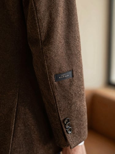A close-up of a premium men's tailored wool blazer sleeve, showing intricate stitching and a genuine designer label tag, warm soft indoor lighting.