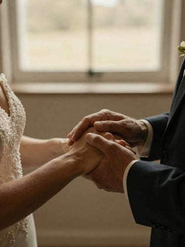 Tight intimate close-up of hands holding during a wedding ceremony, soft natural window light, warm earth tones, cinematic shallow depth of field.