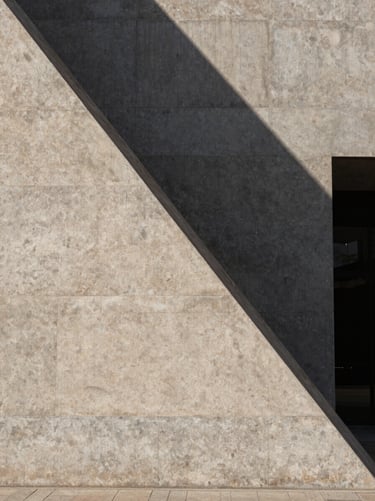 Minimalist architectural geometry of a stone building facade in Madrid, harsh midday shadows cutting diagonally across the concrete panels