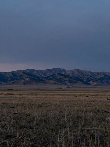 Expansive wide shot of the Wyoming plains under a low-light, moody twilight sky, distant mountains, grounded and quiet.