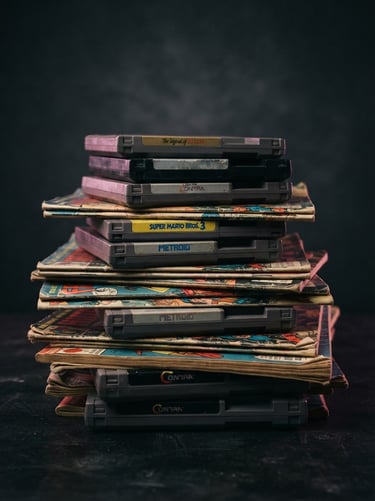 A curated stack of vintage game cartridges and retro comic books, illuminated by a subtle pink rim light on a dark charcoal background.