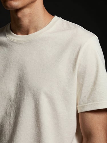 Close-up of a premium off-white t-shirt on a model, high-contrast studio lighting, highlighting the refined cotton weave, 85mm lens
