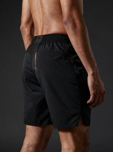 Model wearing matte black technical performance shorts, dramatic side lighting highlighting fabric flexibility, minimalist studio setup, 85mm lens