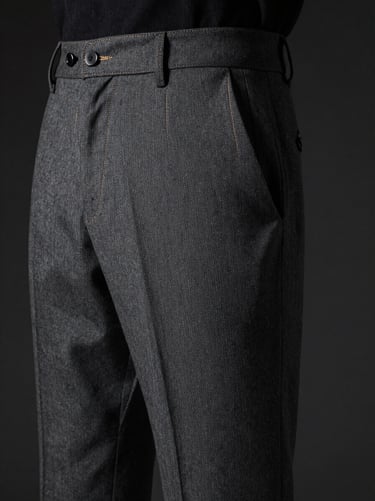Close-up studio shot of charcoal grey tailored trousers, highlighting the precise stitching and premium fabric drape, masculine editorial style, moody lighting, dark background.