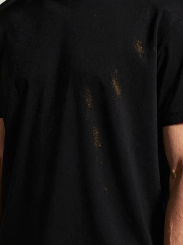 masculine editorial fashion photography, high-contrast studio lighting, deep blacks with subtle gold highlights, sharp focus, 85mm lens. Close-up on the fabric texture and clean stitching of a premium black t-shirt.