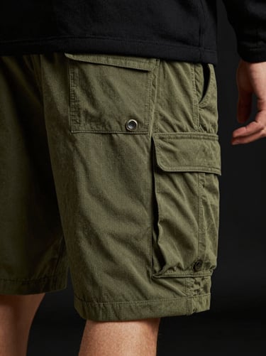 Model wearing olive green utility cargo shorts, moody directional lighting, focus on clean pocket design and durable canvas fabric, 85mm lens