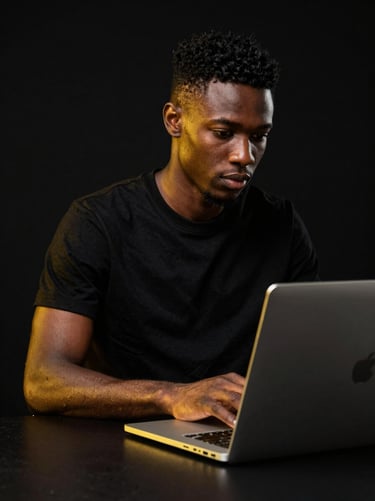 Studio portrait of a focused young African tech professional working with a sleek laptop, dramatic high-contrast lighting, gold accents