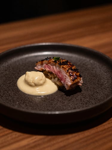 Close-up detail of a beautifully plated signature dish on a dark ceramic plate, warm low-key evening ambient light, shallow depth of field, 35mm
