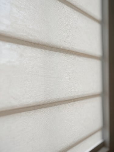 Close-up detail of a white roller blind fabric panel, tight weave texture visible, soft north-facing daylight raking across the surface, no people