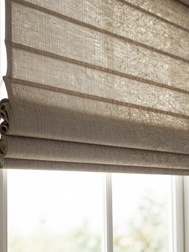 Wide environmental shot of a Roman shade in warm linen fabric, softly folded, hanging in a window with diffused morning light filtering through, empty room, no people