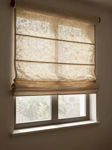 Wide environmental shot of a Roman shade in warm linen fabric, softly folded, hanging in a window with diffused morning light filtering through, empty room, no people