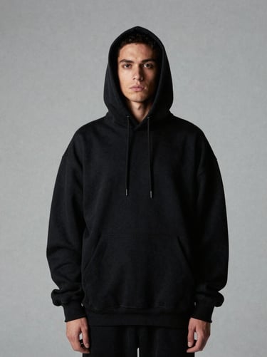 Stark editorial portrait of a model wearing a heavy oversized black hoodie, desaturated grey studio backdrop, cold high-contrast studio lighting, 2:3 aspect ratio