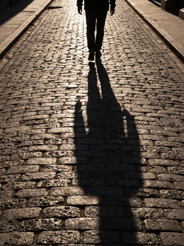 High-contrast shadow of a lone walker on a textured cobblestone alley during sunset, long dramatic lines.