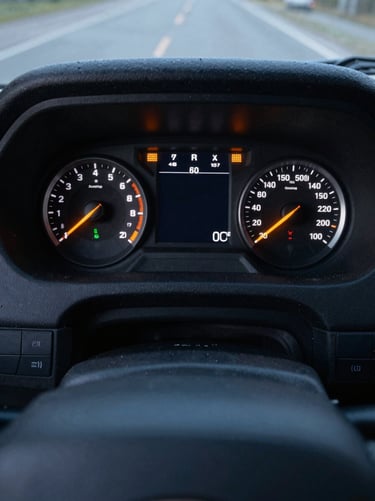 Overhead close-up of a Scania truck dashboard instrument cluster in a dark cab, orange fault warning light illuminated on the display, cool ambient light, no driver visible, forensic framing