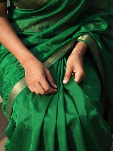 Close-up of hands feeling the heavy-drape raw silk fabric of a deep emerald green saree, sharp details of textile weave under dramatic sunlight, 35mm.