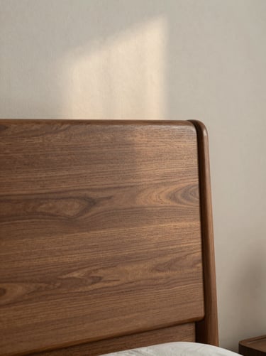 A minimalist solid walnut headboard against a textured plaster wall, soft morning side-light, 35mm