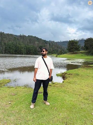Traveler at the serene shore of Poondi Lake in Kodaikanal, surrounded by calm waters and rolling green hills.