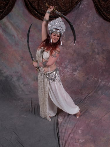 Bellydancer Shahravar with double swords wearing white assuit costume with coin bedlah