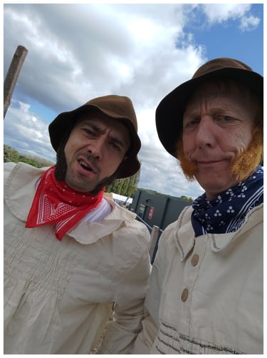 Two men in vintage 19th-century peasant costumes with sideburns and bandanas at a historical reenactment.