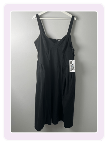 A black sleeveless midi dress by Future Collective hanging on a white hanger against a gray wall.