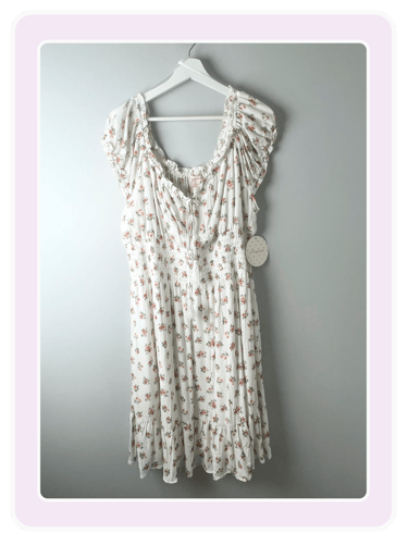 White cottagecore dress with pink floral print, ruffled sleeves, and smocked waist on a hanger.