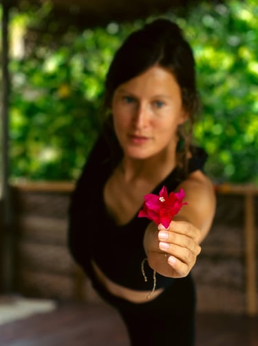 Yoga teacher in dancer pose holding flower with focus on blossom, mindful essentials