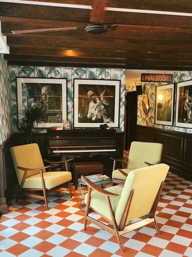 Mid-century modern jazz lounge featuring lime green armchairs, a piano, and tropical palm wallpaper.