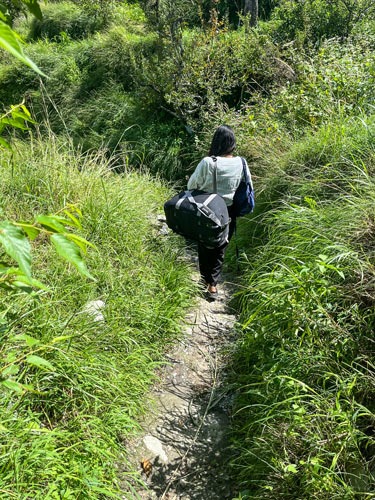 Pooja with large bag going down steep path.