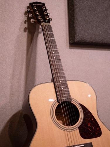A moody close-up of an acoustic guitar leaning against a textured wall in a Venezuelan recording studio, warm antique white and dusty rose lighting, authentic musical atmosphere.
