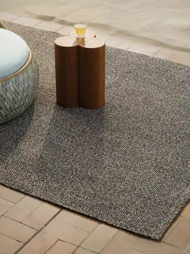 Outdoor rug adding soft texture to a balcony reading corner with natural tones and cozy outdoor styl