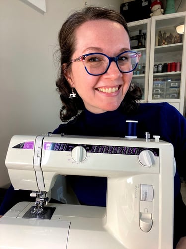 Close-up of a woman with glasses and brown hair smiling behind a sewing machine.