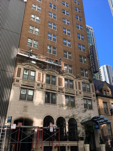 Masonry repair on the facade of a classic brick building using a suspended scaffold.