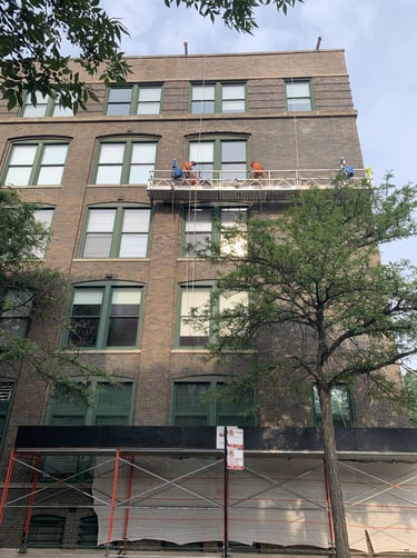 Masonry crew on scaffolding restoring the facade of a large brick apartment building.
