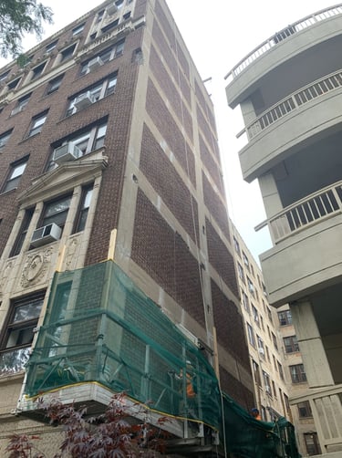 Facade repair on a brick and concrete building with scaffolding and green safety netting.