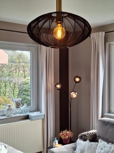 Un luminaire allumé en tissu noir devant un mur beige et des panneaux décoratifs bruns