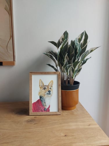 Framed A5 colored pencil dog portrait on a table next to a plant