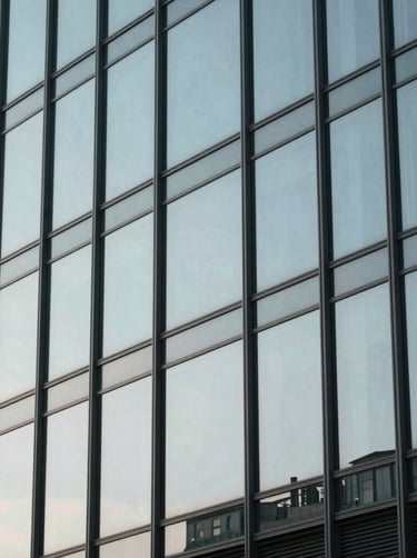 Clean street photography of a modern glass building reflecting a pale silver blue sky, minimalistic composition with sharp geometric lines, International / Western.