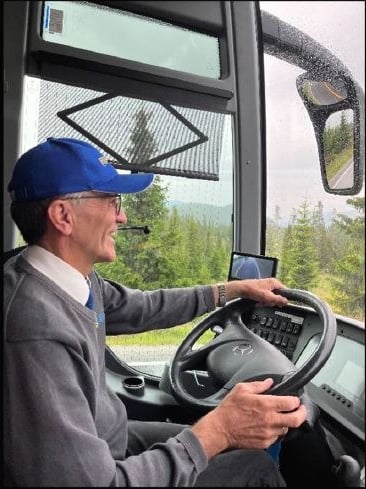 a smiing man in profile with a blue hat driving a bus