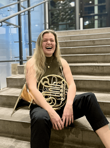 Delaney Breen sitting on a stair case with her french horn
