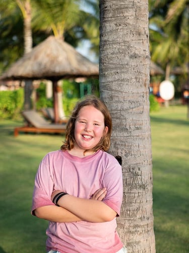 Individual portrait of a boy smiling by a palm tree during a family photoshoot at Mövenpick Resort P
