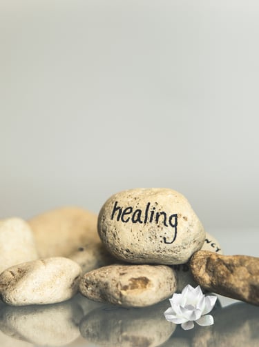 A zen stack of smooth river stones with 'healing' written on one, beside a white lotus flower.