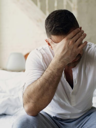 Stressed man sitting on bed with head in hand during a relationship conflict.