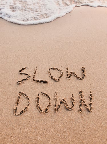 The words slow down written in the sand on a tropical beach with ocean waves.